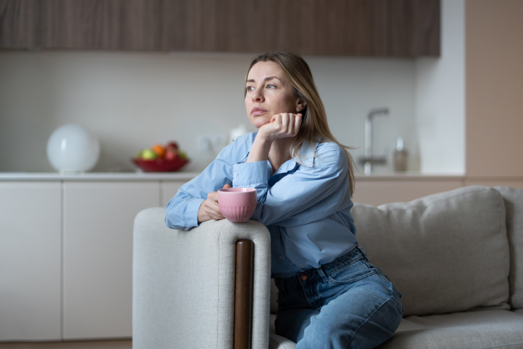 Slightly sad middle aged woman sitting on home couch looking bored