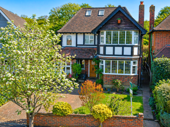 Two-story Tudor-style house with black-and-white timber framing, a large bay window, and a brick base, front garden full of plants.