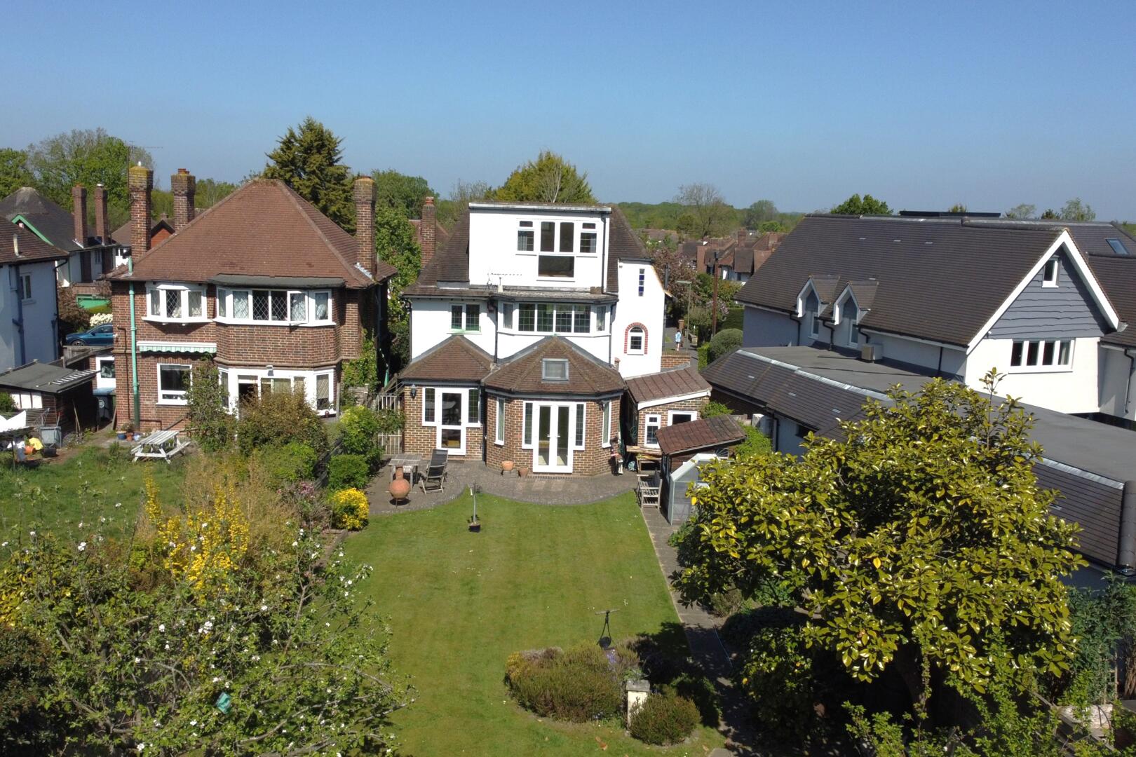 Aerial view of a suburban neighborhood with brick and white houses, pitched roofs, and a central green lawn seen from above on a clear day in spring/fall-season light.