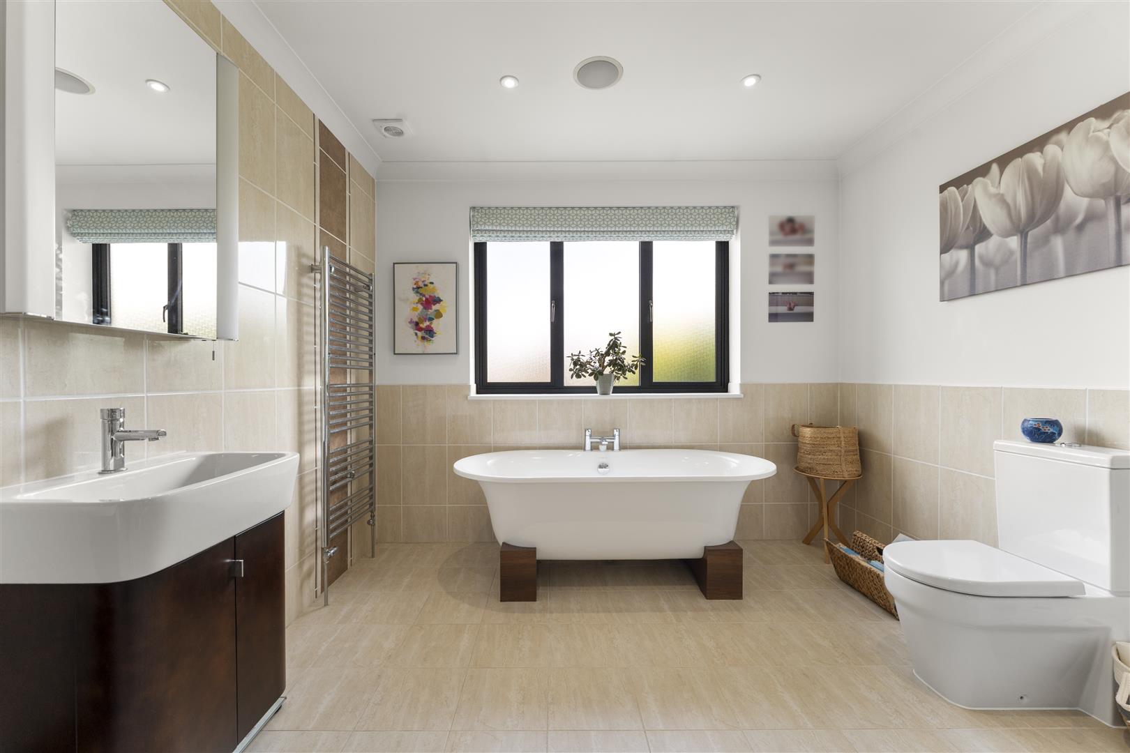 Modern bathroom with freestanding white tub on wooden supports, beige tiled walls, and a vanity with sink on the left.
