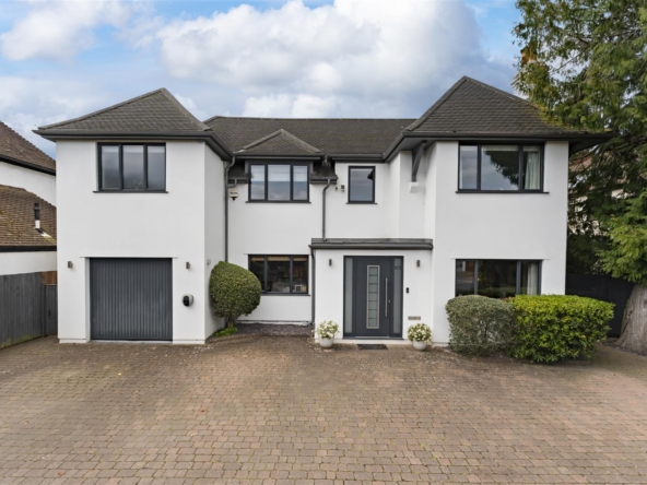 White two-story house with a grey roof and attached garage, front door centered between trimmed shrubs on a brick driveway.