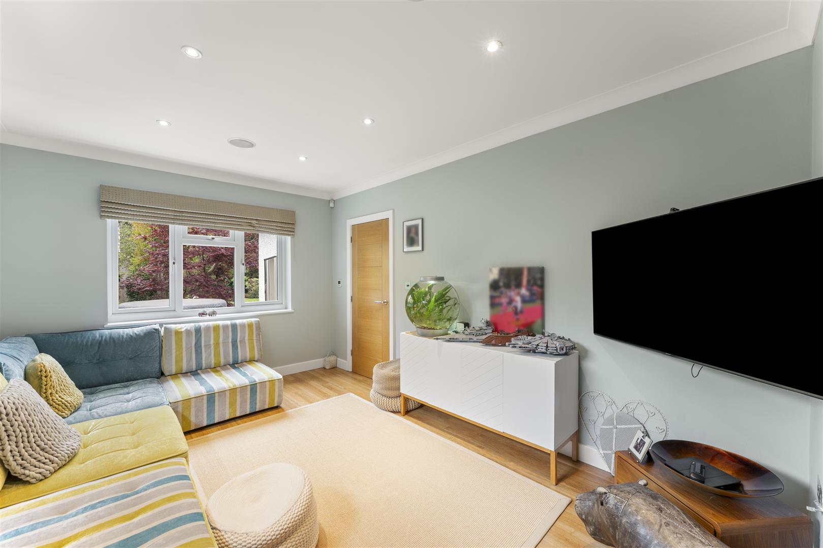 Bright living room with pastel walls, a striped sofa, and a wall-mounted TV on the right side.
