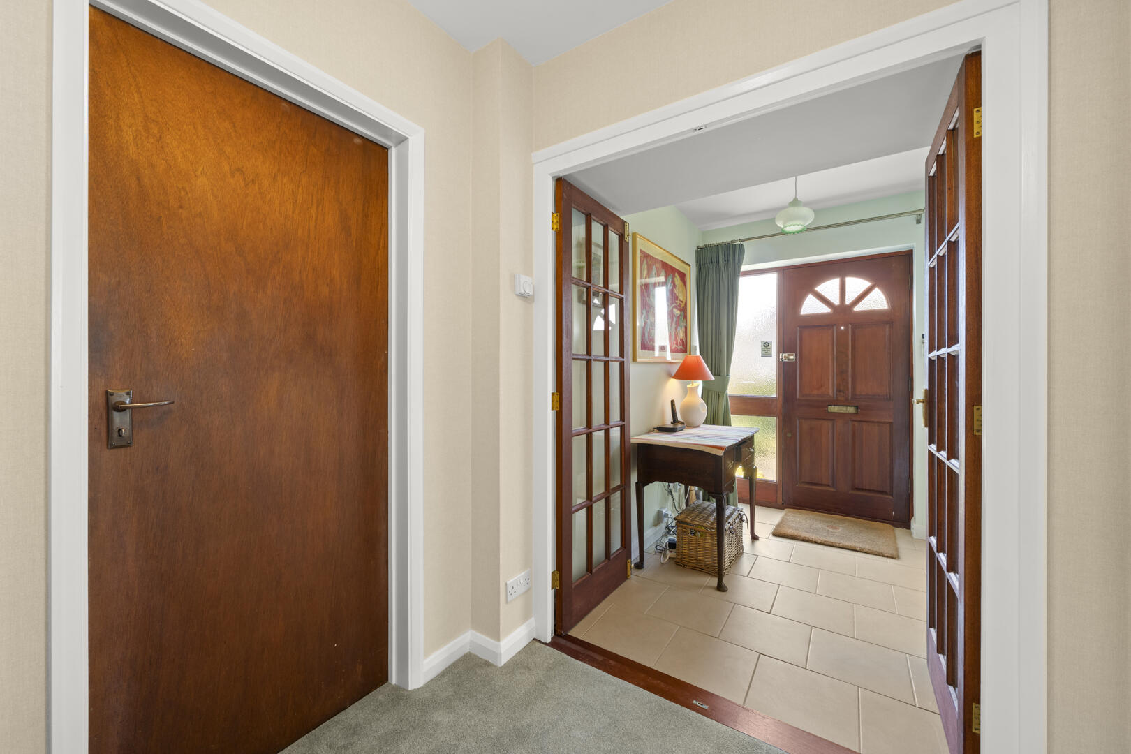 Interior hallway opening into a sunny foyer with a wooden front door and a console table by the entryway