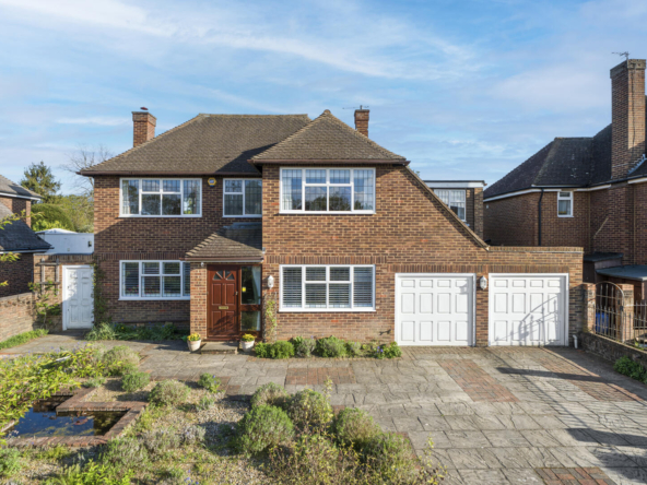 Two-story brick house with a double garage, brown front door, and a paved driveway framed by low shrubs.