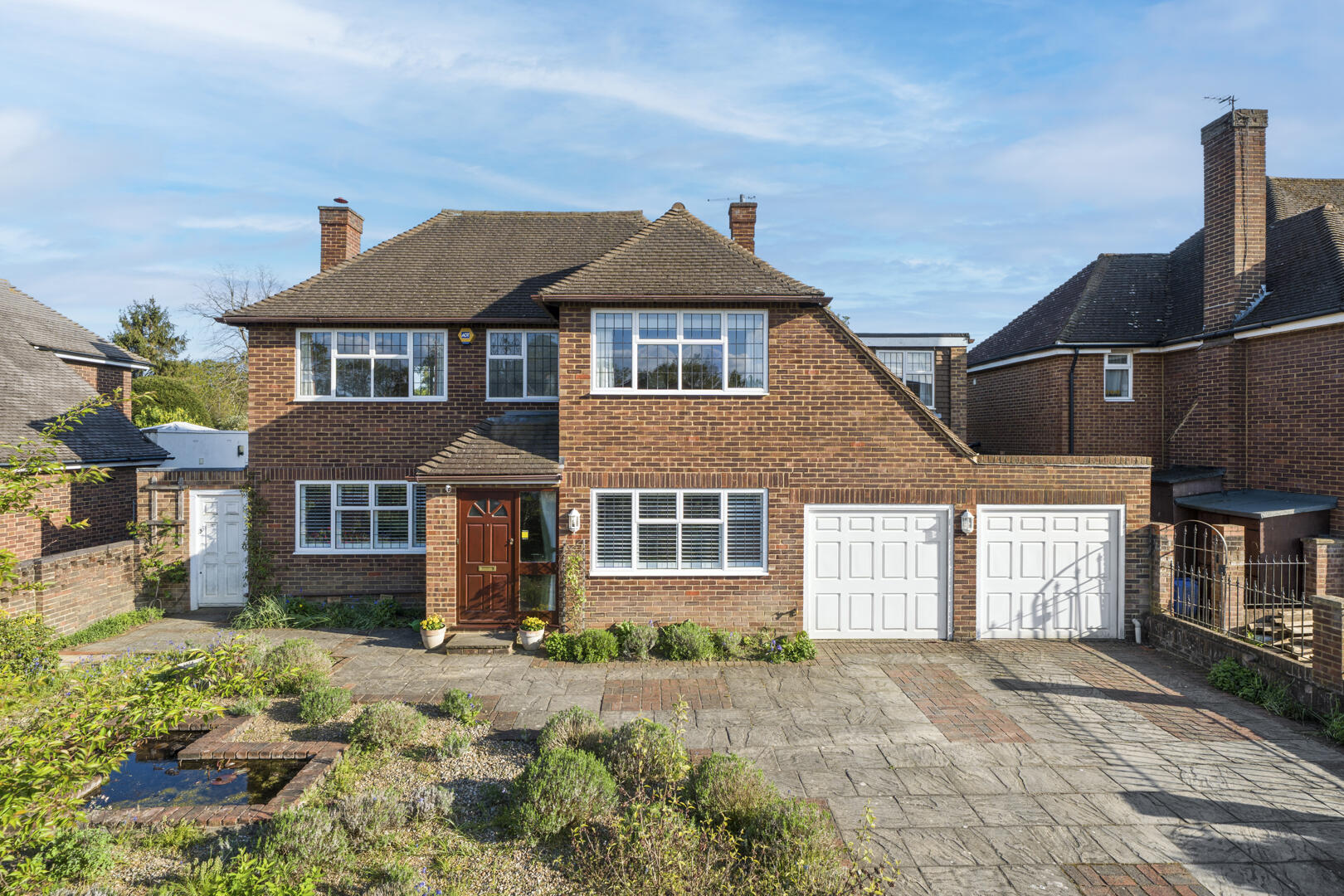 Two-story brick house with a double garage, brown front door, and a paved driveway framed by low shrubs.