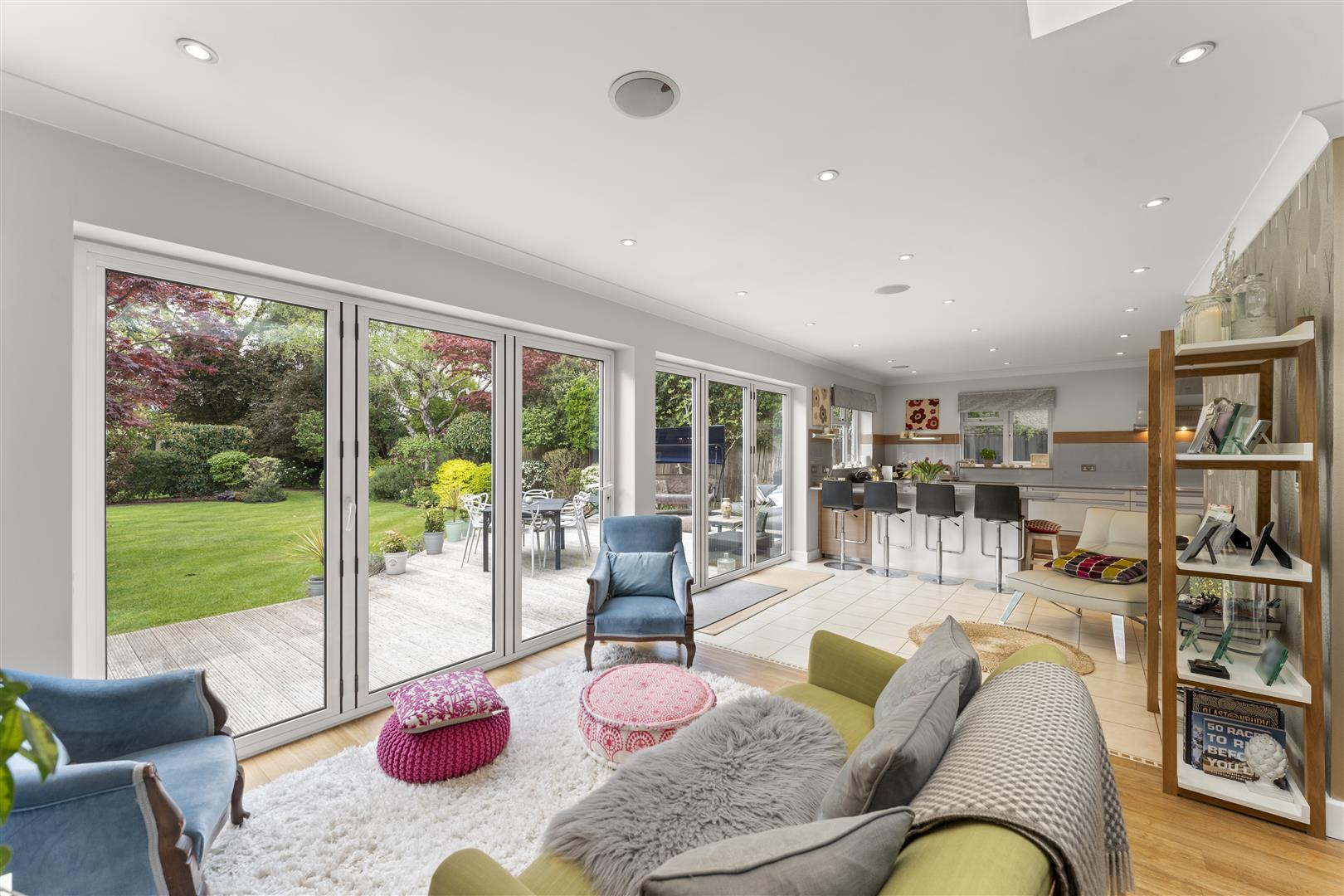 Open-plan living room and kitchen with floor-to-ceiling glass sliding doors opening to a green backyard deck.