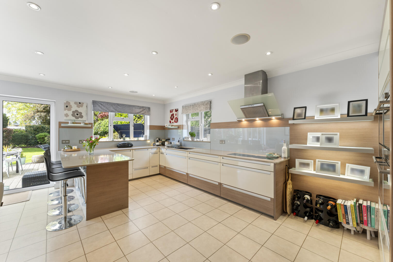 Bright contemporary kitchen with a central island, white cabinets, and stainless steel range hood under a light ceiling, plus shelves with framed photos on the wall.