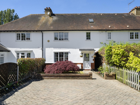 White two-story house with a red-tiled roof, front garden with a red shrub, and a paved driveway under a blue sky