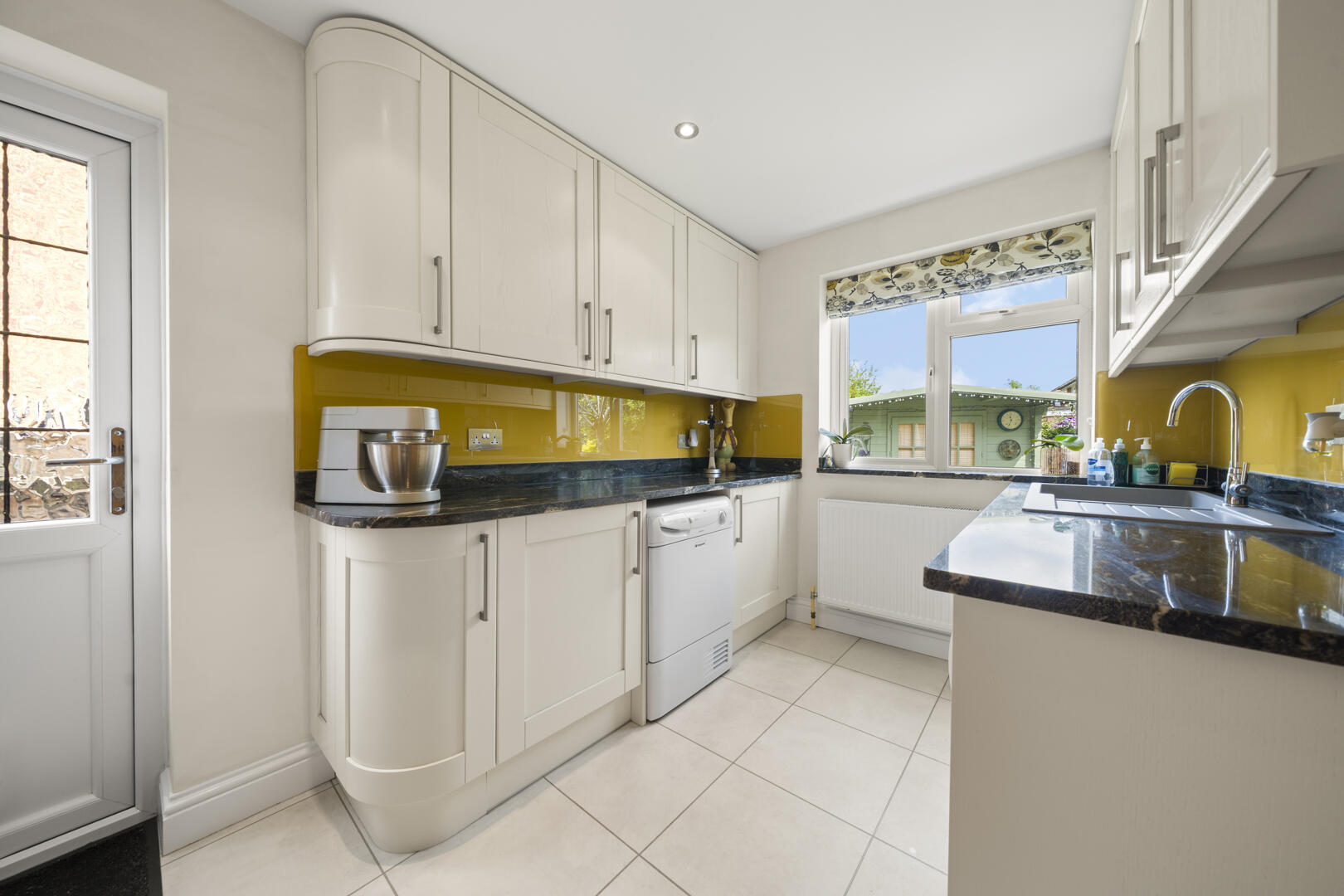Bright, modern kitchen with white cabinets, yellow glass backsplash, and dark countertops; dishwasher under the counter and a stand mixer on the left.