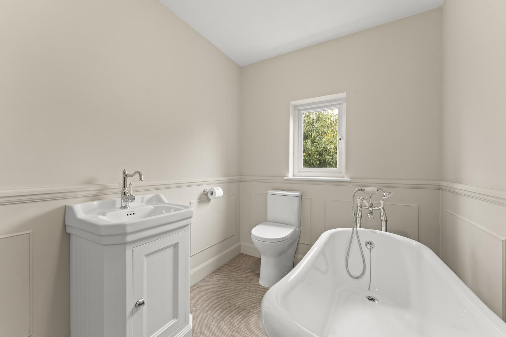Bright white bathroom with a pedestal sink, toilet, and a white freestanding tub under a small window.
