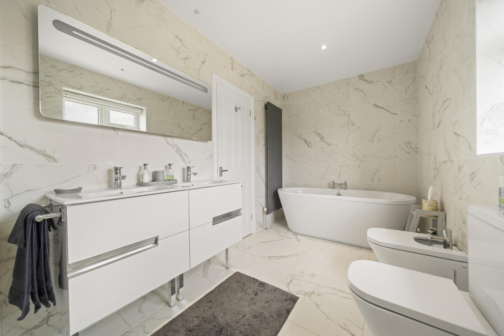 Modern white bathroom with a double vanity, large wall mirror, and marble-tiled walls and floor