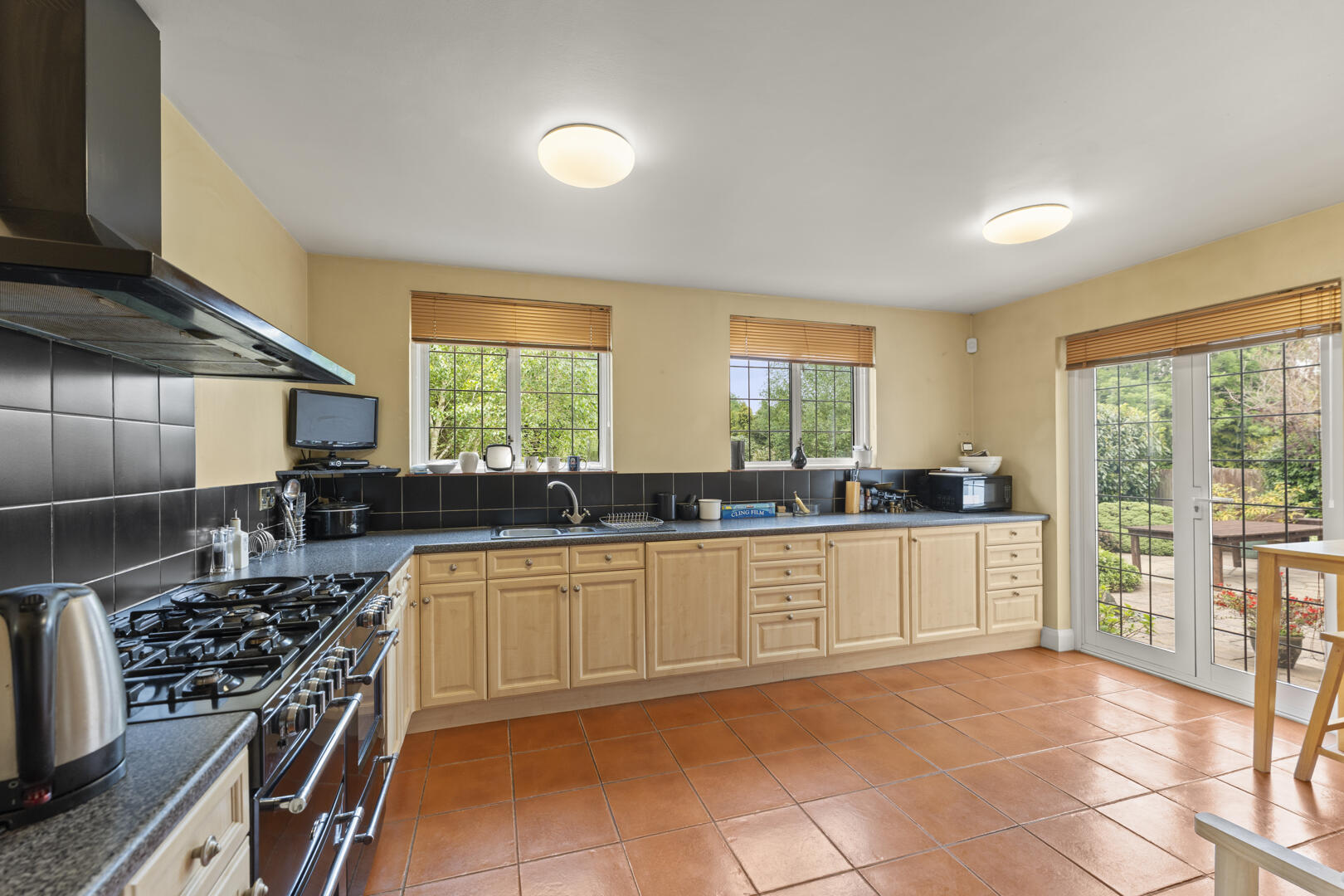 Bright kitchen with beige cabinets, black tiled backsplash, and a large glass door opening to a garden patio.