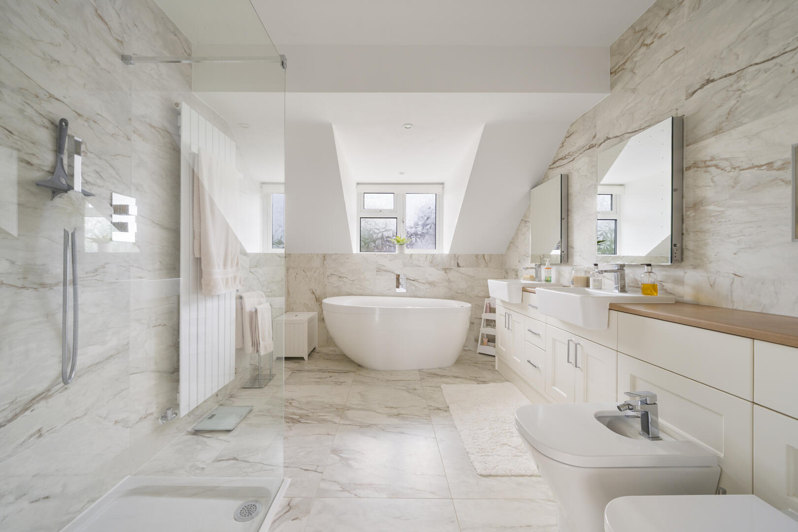 Luxurious white marble bathroom with a freestanding tub under a skylight and a double vanity on the right, bathed in natural light