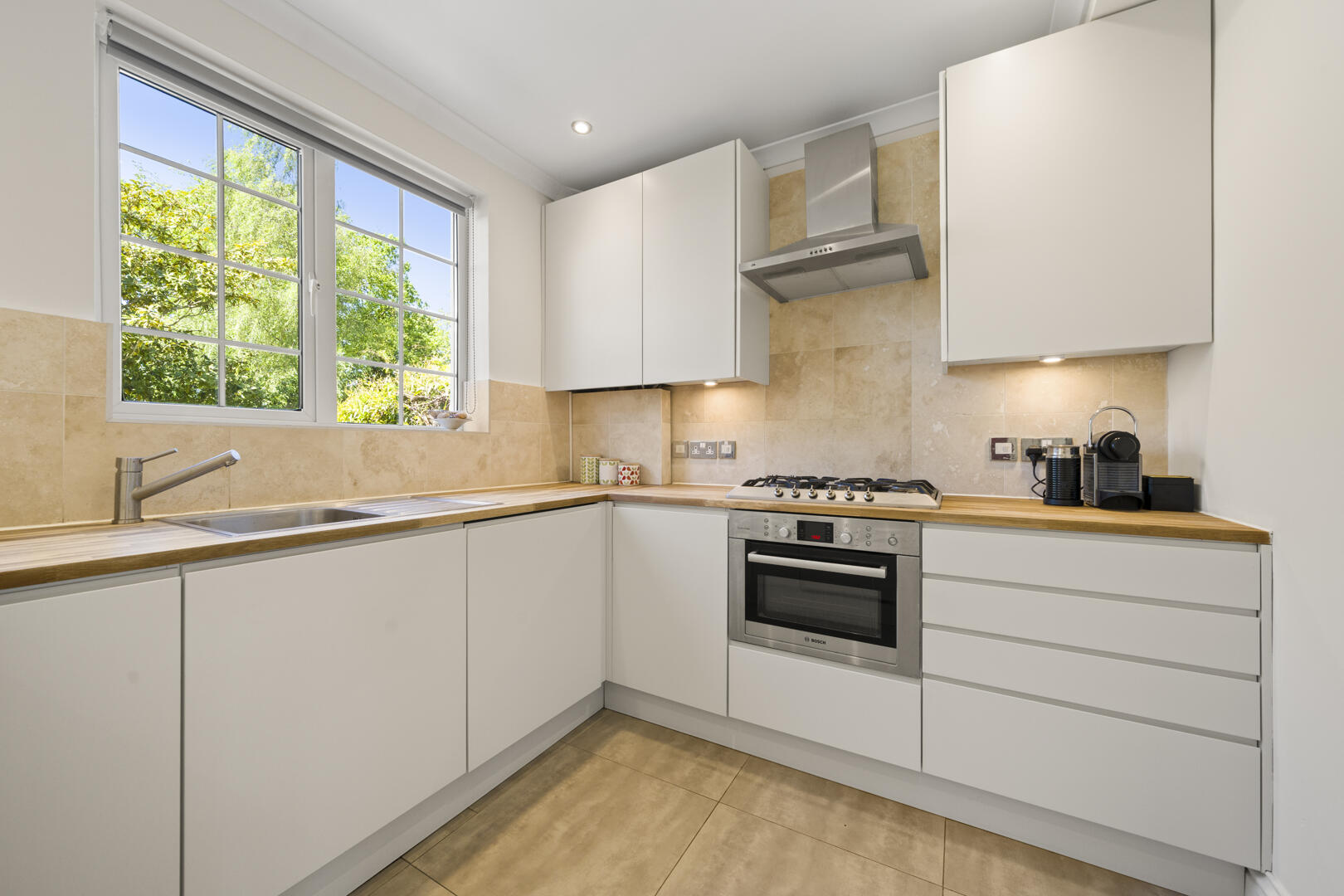 Bright modern kitchen with white cabinets, beige tile backsplash, and a window above the sink.