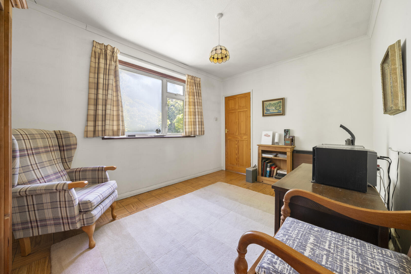 Cozy home office with plaid armchairs, a sunlit window with checkered curtains, and a wooden desk with a printer.