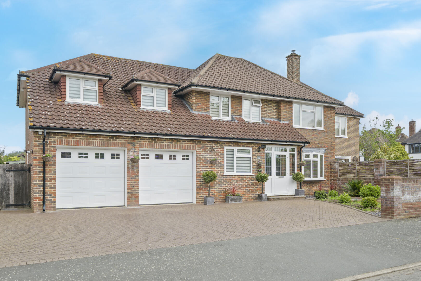 Front view of a brick house with tiled roof, dormer windows, and a double garage.
