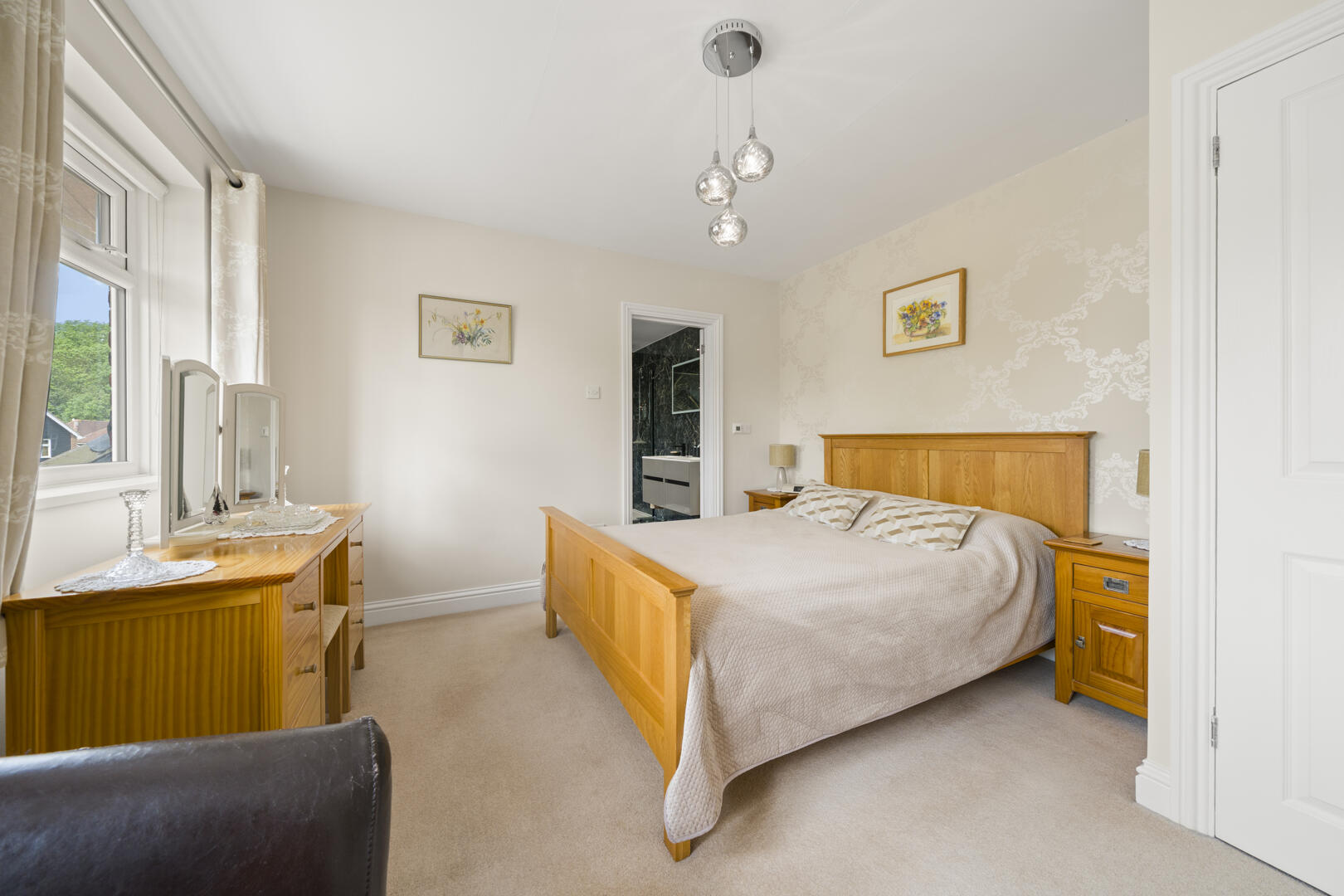 Bright bedroom with a large wooden bed, matching nightstands, beige quilt, and an upholstered window curtain wall.