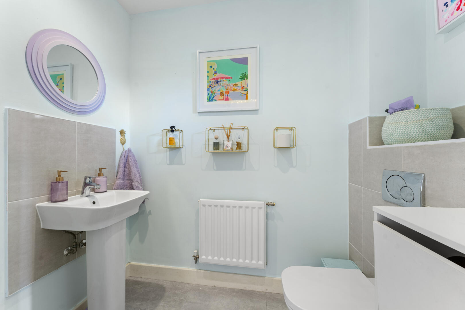 Light blue bathroom with wall-mounted pedestal sink, lavender soap dispensers, and a matching towel hanging by the sink.
