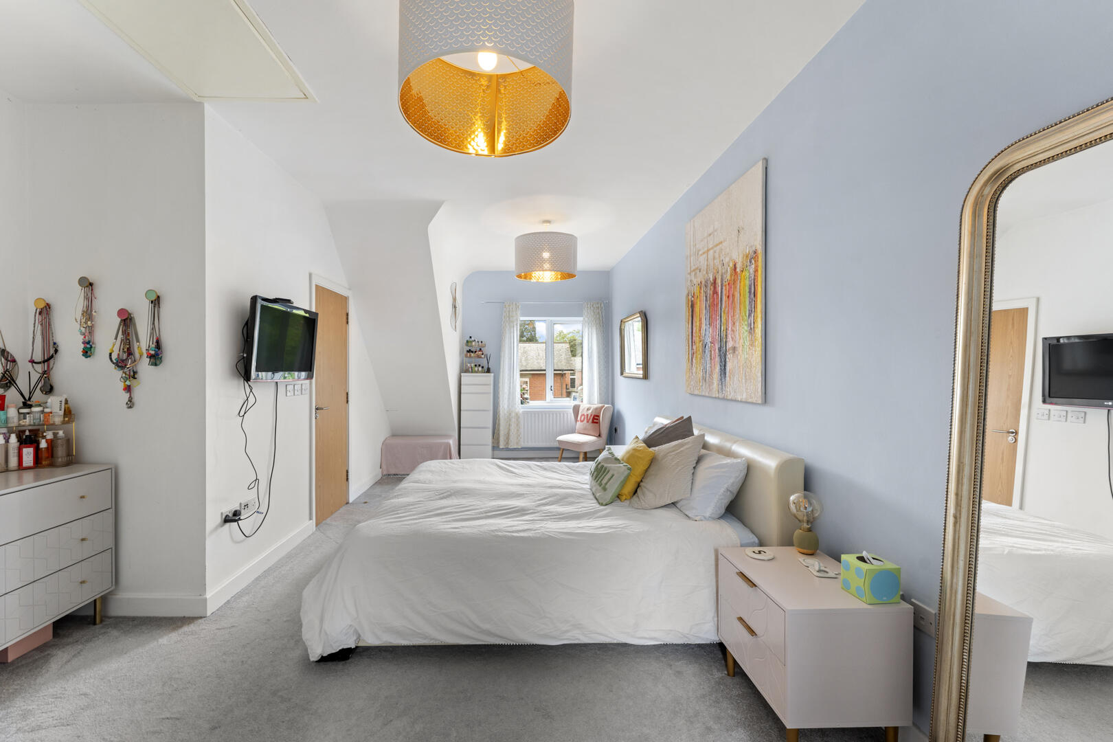 Bright bedroom with a white bed centered, blue accent wall, and a large ornate mirror along the right wall.