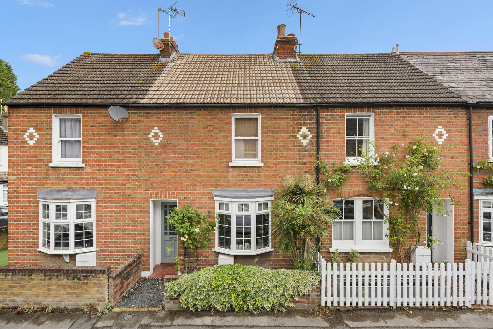 Red brick terraced house with white diamond decorative motifs, bay windows, and a small front garden.