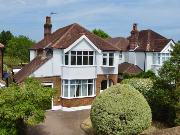 Row of white, red-brick houses with bay windows and red-tiled roofs, flanked by green hedges and trees in a sunny neighborhood court