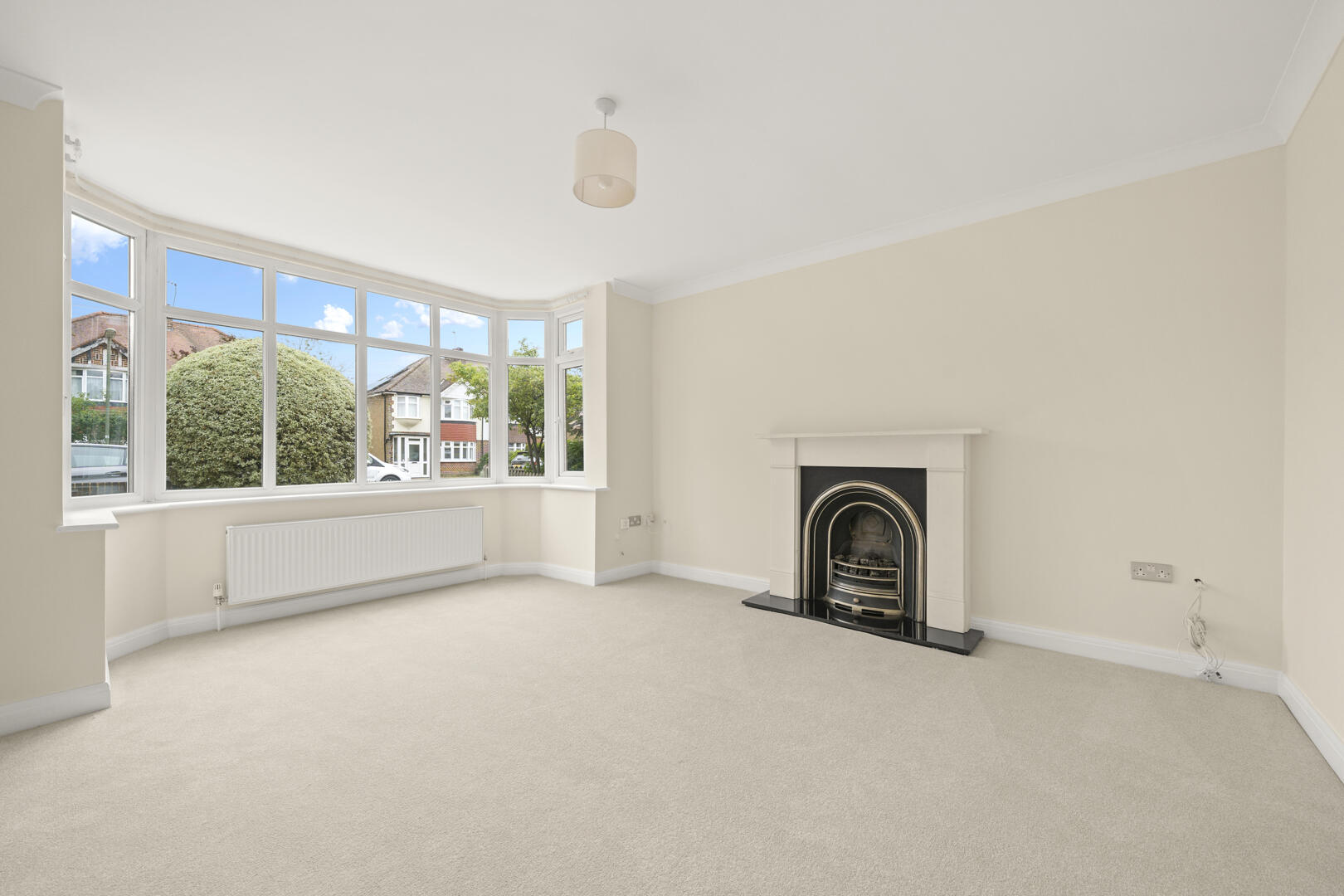 Bright living room with a curved bay window, radiator, beige walls, and a decorative fireplace on the right.