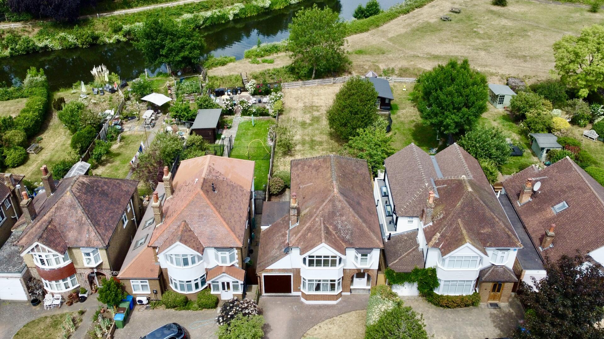 Aerial view of a row of brick terraced houses with pitched roofs; backyards show gardens, sheds, and a river running along the top edge.