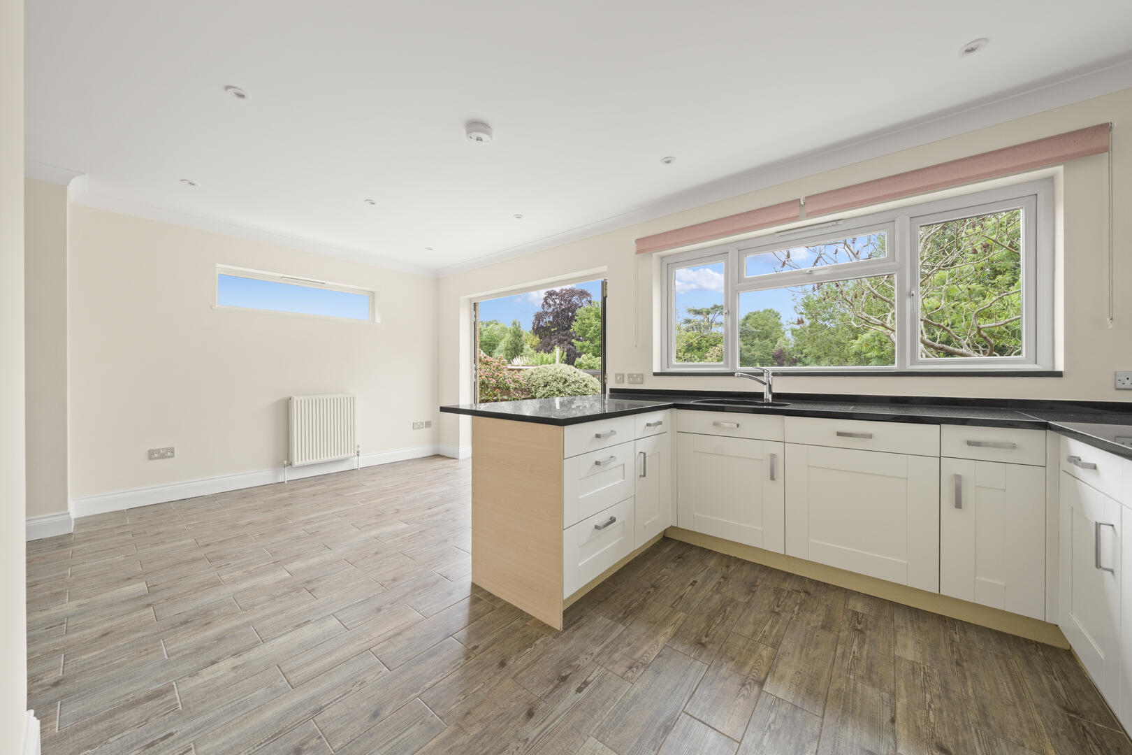 Bright modern kitchen with white cabinets, black countertops, and a large window overlooking greenery.