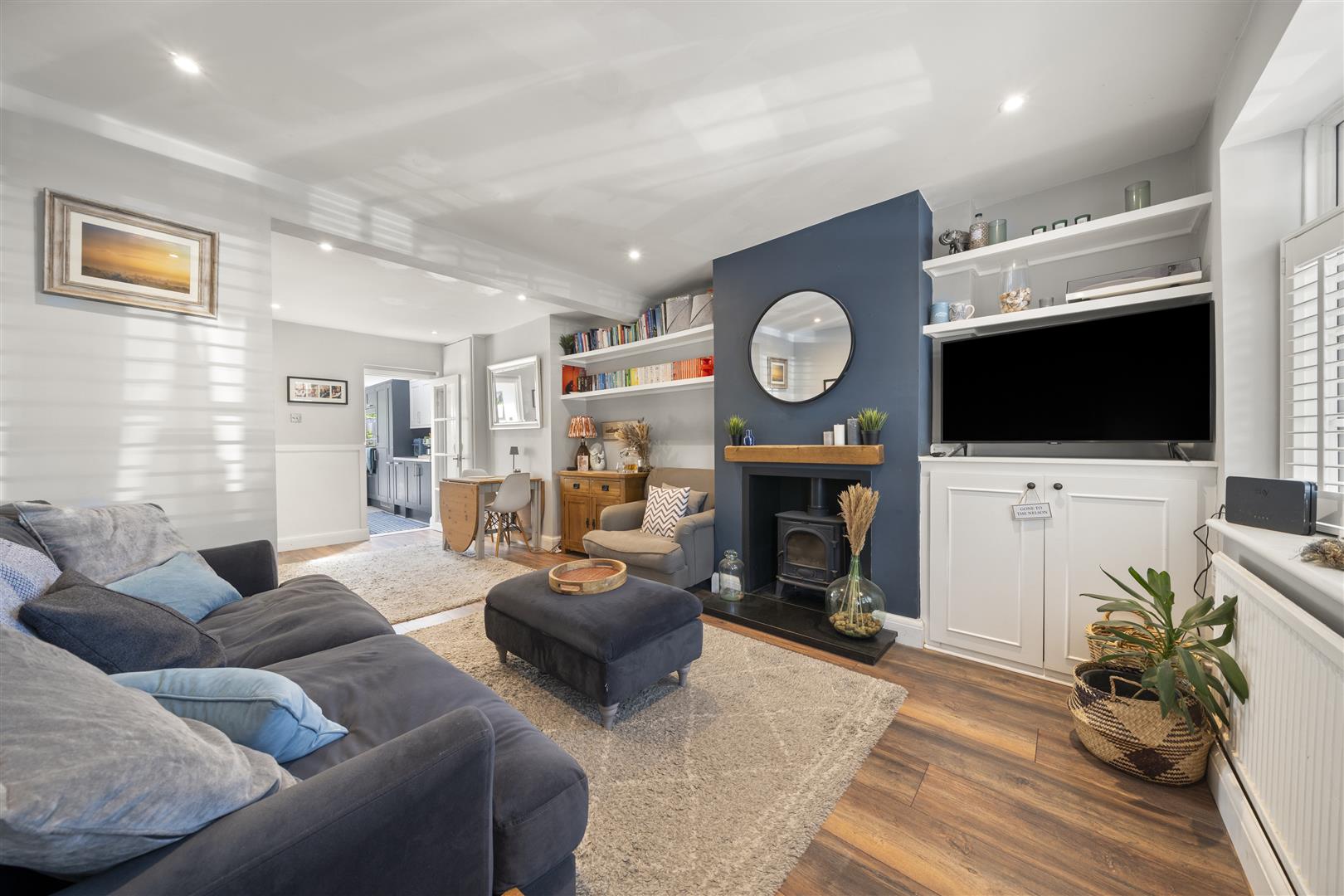 Open-plan living room with a gray sofa, blue accent fireplace wall, round mirror, and built-in shelving.