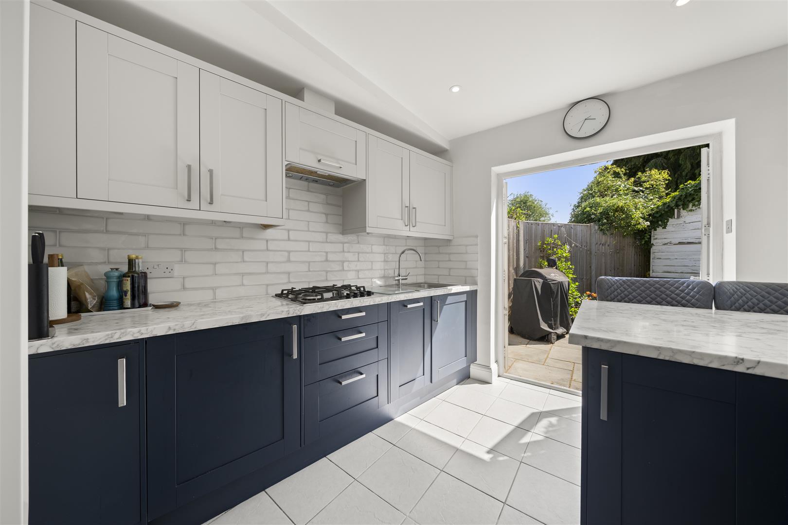 Modern kitchen with white upper cabinets, navy lower cabinets, marble countertops, and a view of the backyard through a glass door.