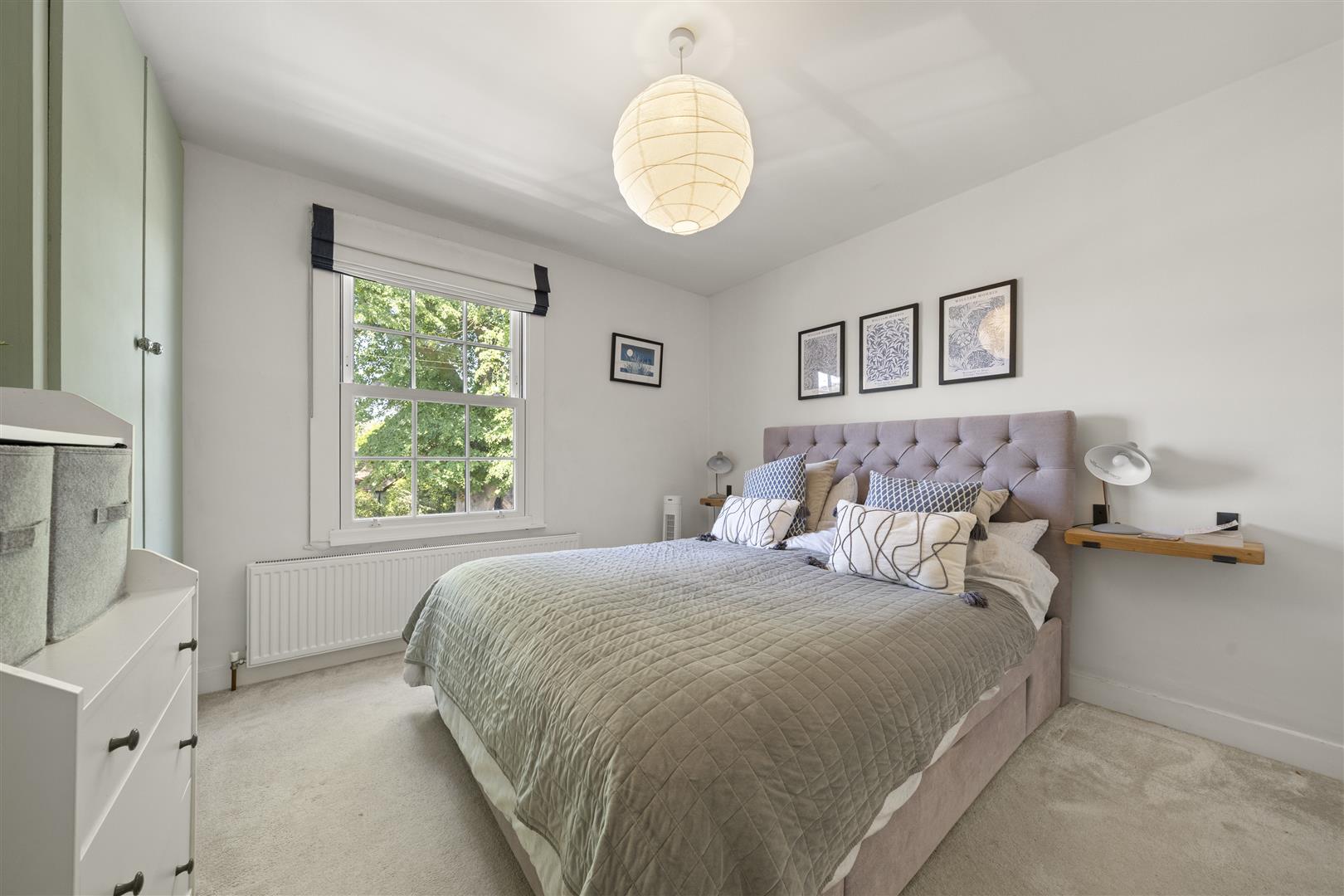 A cozy bedroom with a tufted lavender bed, matching quilted bedding, and decorative pillows, flanked by wall shelves and framed art above the headboard.