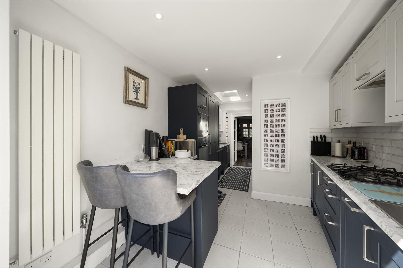Modern kitchen with navy cabinets, white marble island, and two gray upholstered bar stools at a breakfast bar.