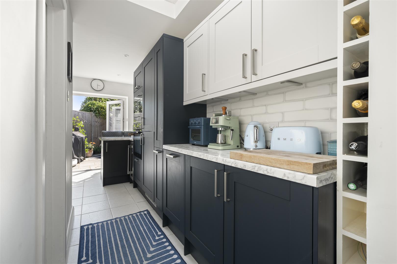 Modern galley kitchen with dark blue lower cabinets, white uppers, and a marble countertop with small appliances on display.