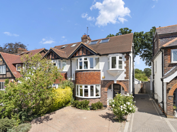 Row of traditional British houses with brick and white plaster, bay windows and red-tiled roofs under a bright blue sky.