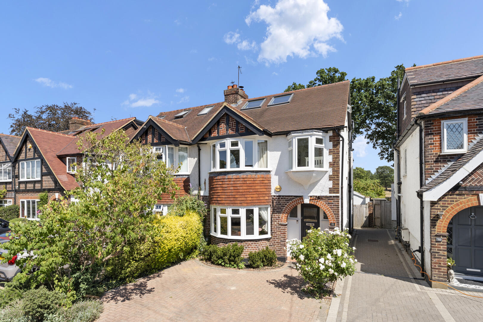 Row of traditional British houses with brick and white plaster, bay windows and red-tiled roofs under a bright blue sky.