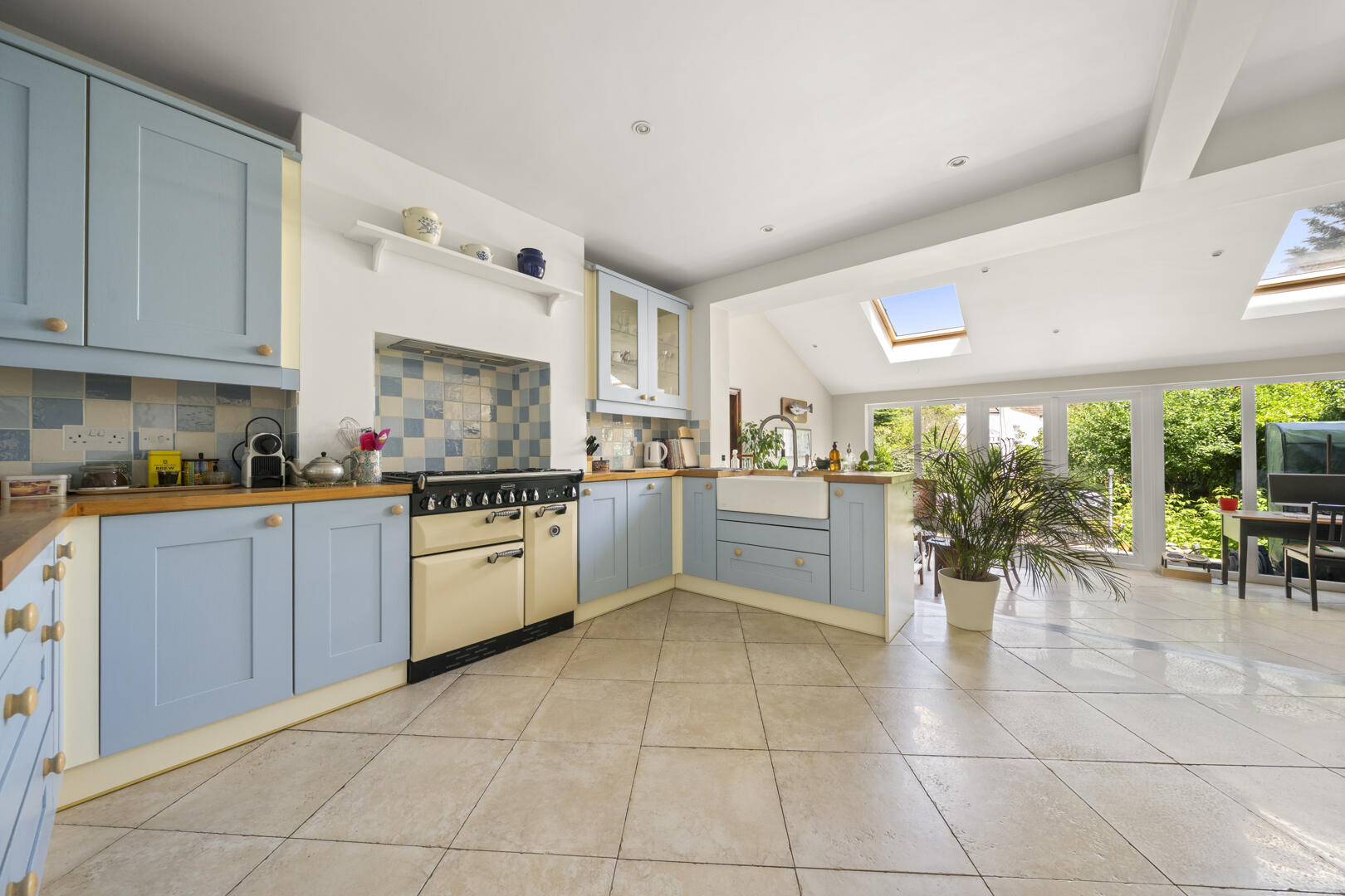 Bright airy kitchen with light blue cabinets, beige tiled floor, and a cream vintage range stove under a blue-and-tile backsplash.