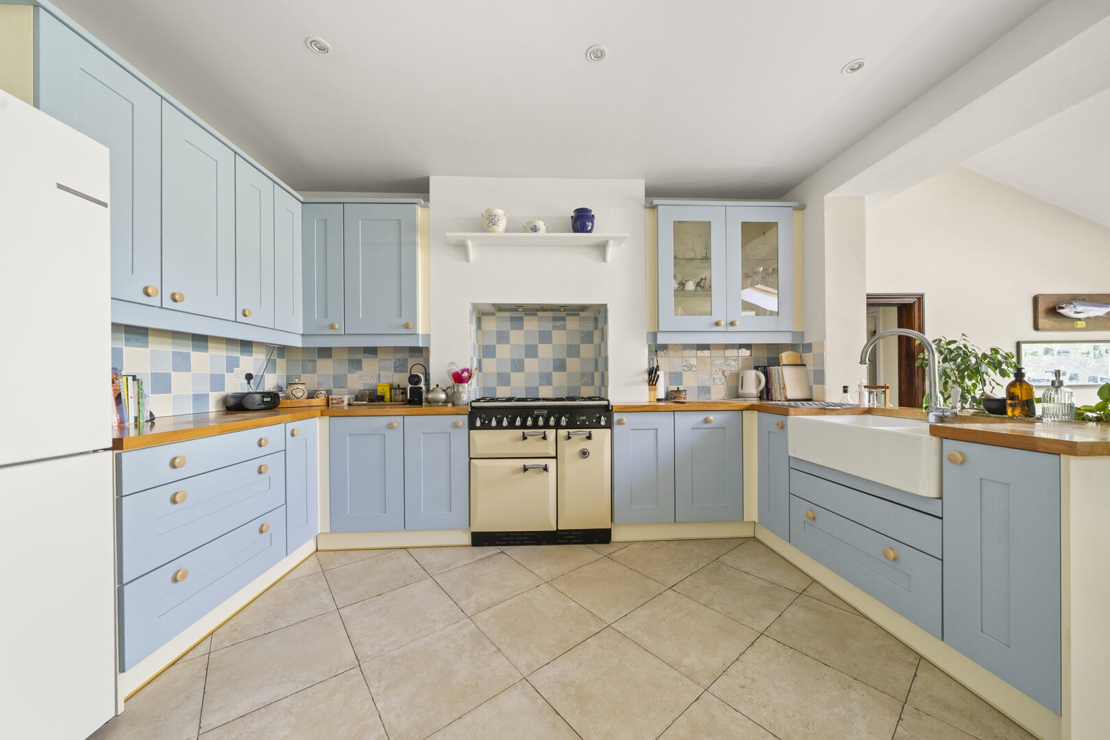 Bright U-shaped kitchen with light blue cabinets, wooden countertops, and a central cream range stove surrounded by a blue-and-white checkerboard backsplash.