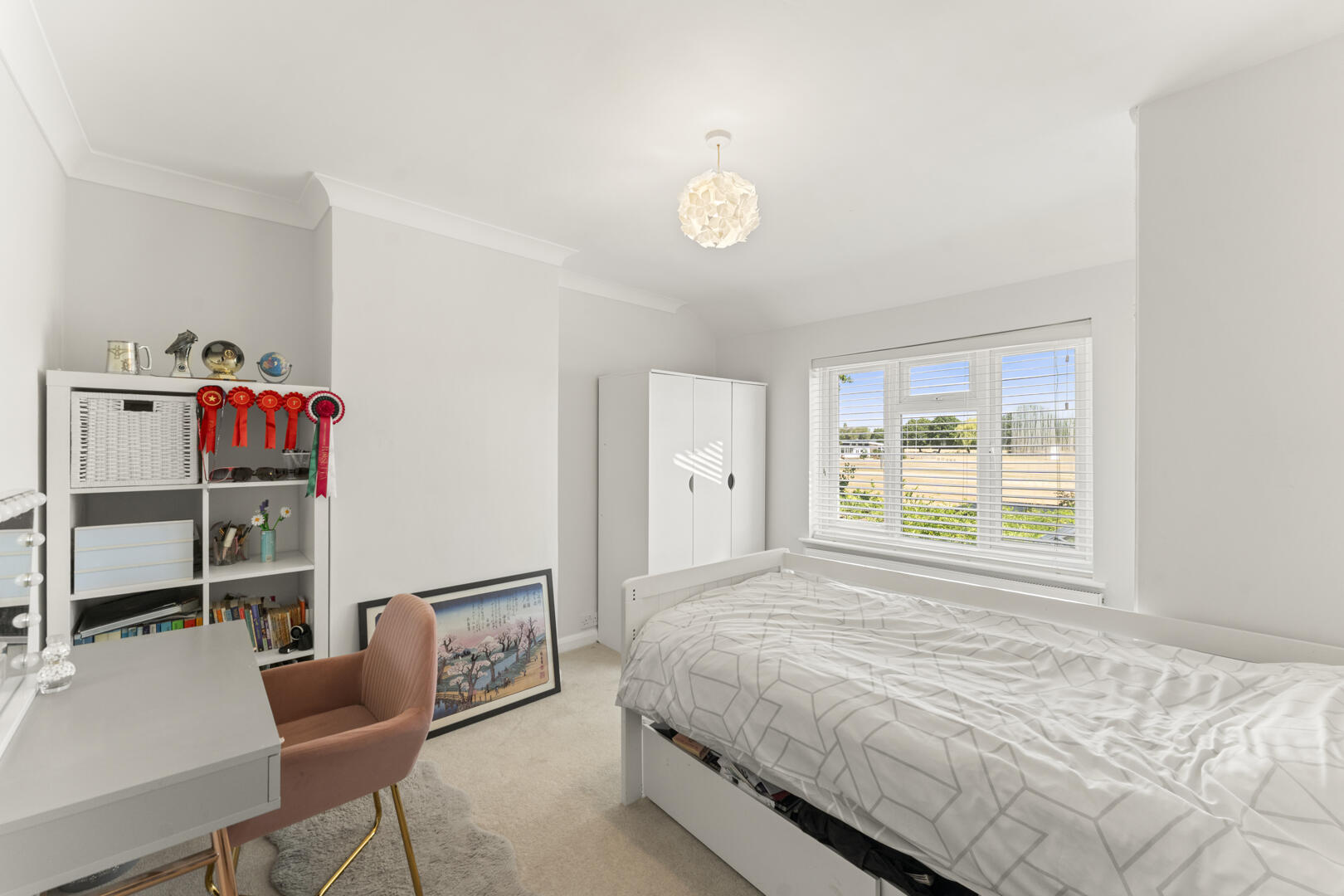 Bright white bedroom with a single bed, white wardrobe, and study desk; ribbons and trophies on a shelf under a sunny window.