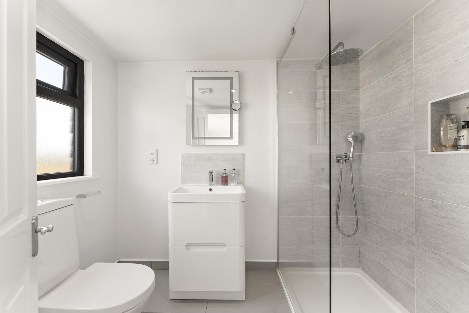 Modern white bathroom with a glass-walled shower, wall-mounted vanity, mirror, and toilet on the left.