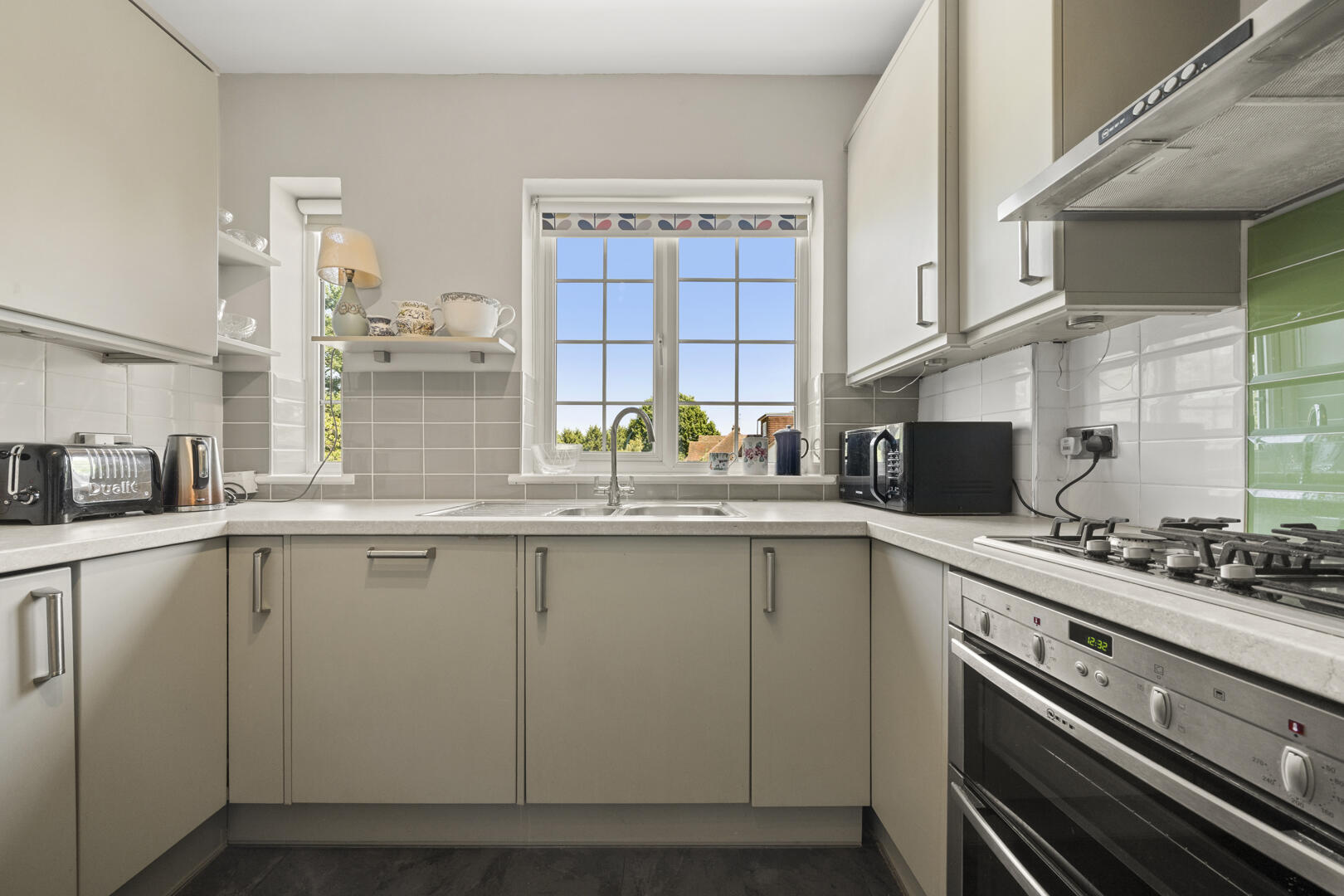 Bright, modern kitchen with gray cabinets arranged in a U-shape, central window above the sink, and a gas stove on the right.