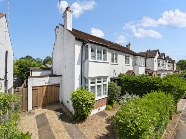 White, two-story houses with bay windows in a residential street, blue sky and hedges in front gardens.