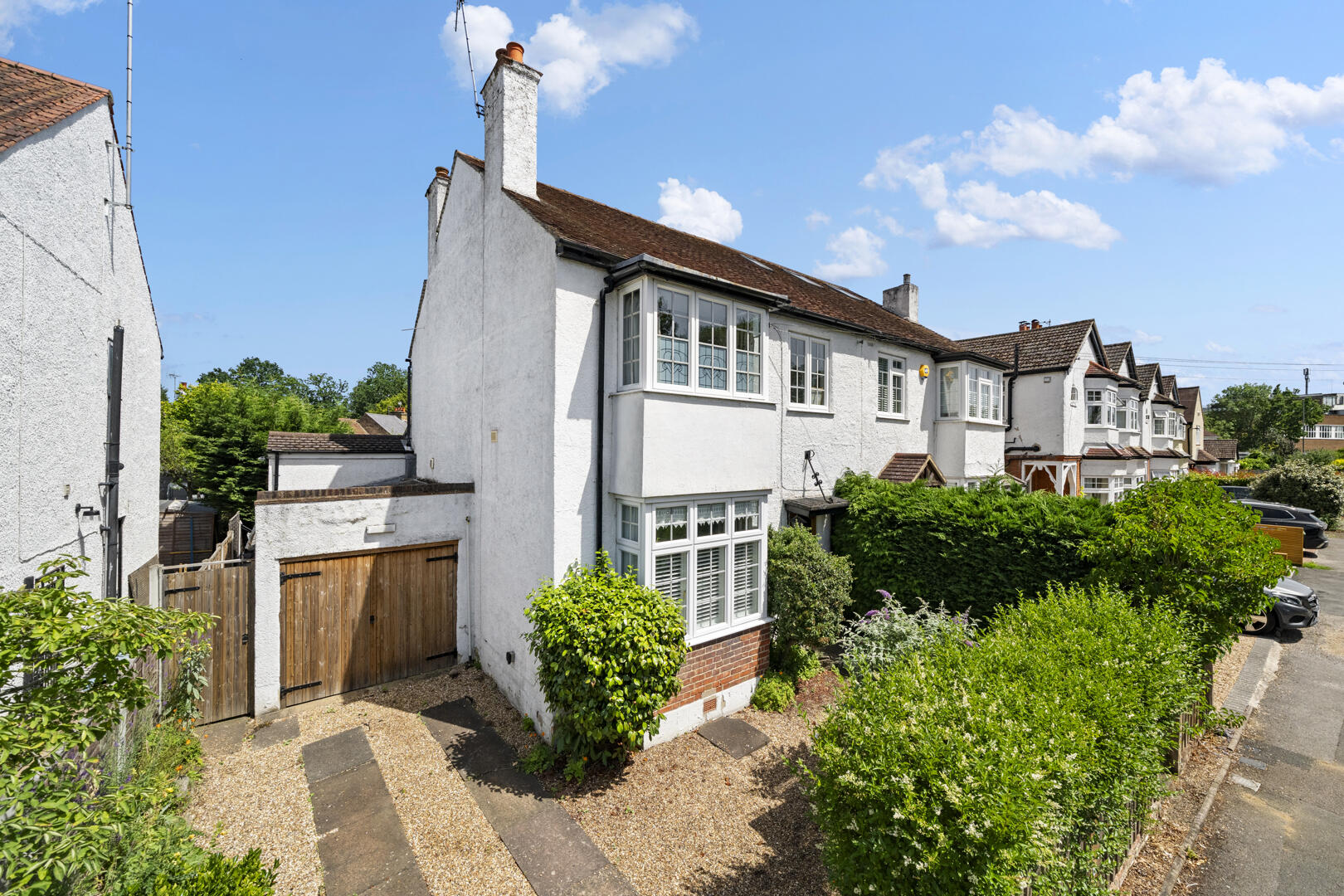 White, two-story houses with bay windows in a residential street, blue sky and hedges in front gardens.
