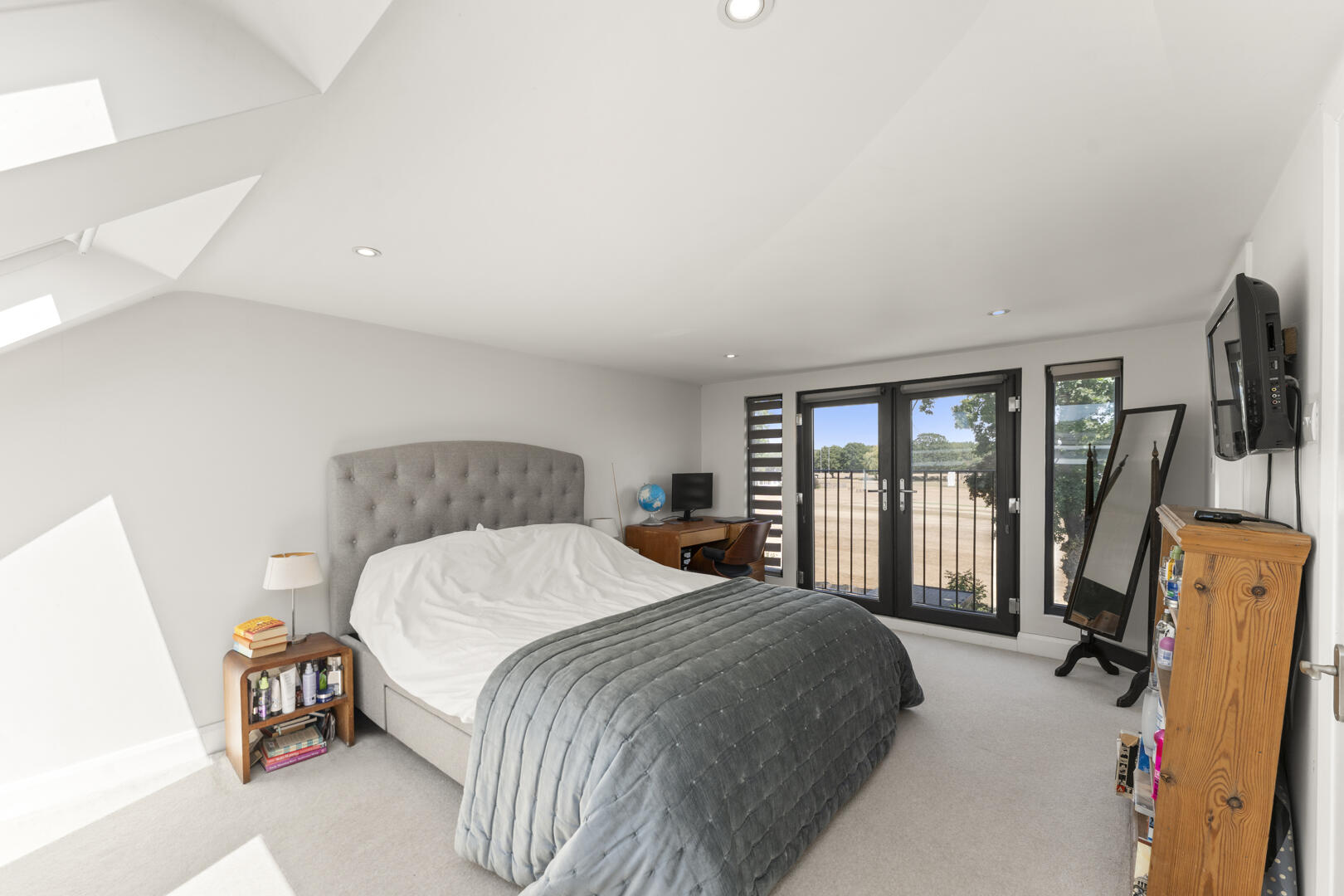 Bright attic bedroom with a large bed and gray upholstered headboard, white linens, and a gray quilt; skylights brighten the room.